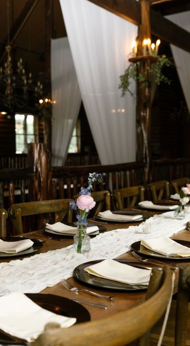Rustic dining table set with plates, napkins, and floral centerpieces in a cozy wooden room.