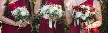 Bridesmaids in red dresses holding elegant white and red rose bouquets.