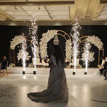Bride standing alone facing decorated floral arches and sparklers.
