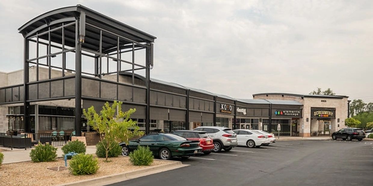 Modern shopping plaza with parked cars and cloudy sky.