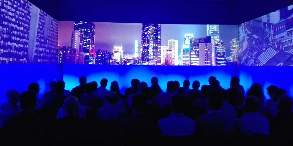 Audience watching a vibrant cityscape projection in a dark room with blue lighting.