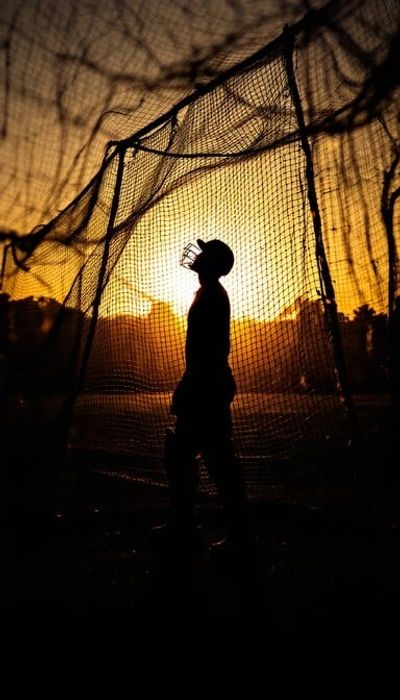 Silhouette of a cricket player in helmet against a golden sunset backdrop.