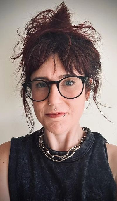 Woman with glasses, piercings, and a chunky chain necklace.