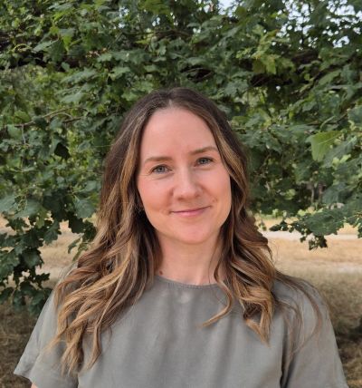 Woman smiling outdoors with leafy background.