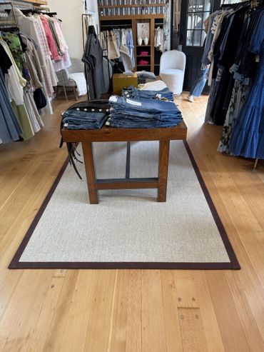 Clothing store interior with jeans on a wooden table and racks of clothes.