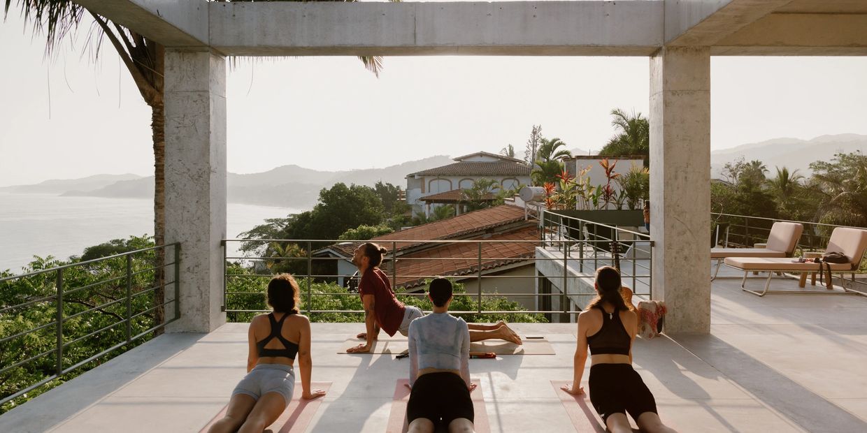 Four people practicing yoga on a terrace overlooking a scenic ocean view.