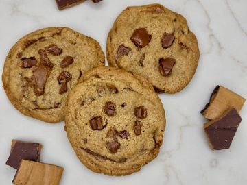 Three chocolate chunk cookies on a marble surface.