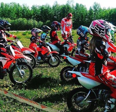 Kids lined up on dirt bikes ready to race with their coach.