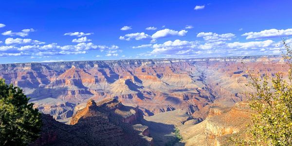 Vast view of the Grand Canyon under a bright blue sky with scattered clouds.