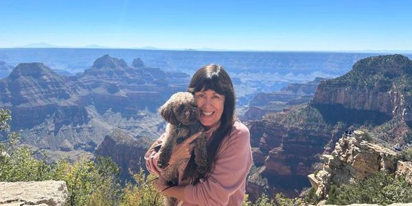 Woman holding a small dog with a scenic canyon backdrop.