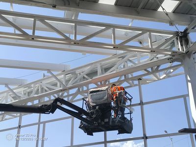 Worker on a lift inspecting a white steel structure under a clear sky.