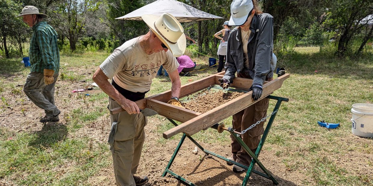 Two people sifting dirt at an archeological site.