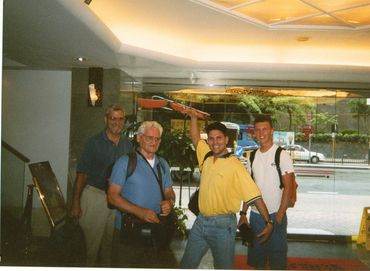 Four men posing happily inside a building near a glass door.