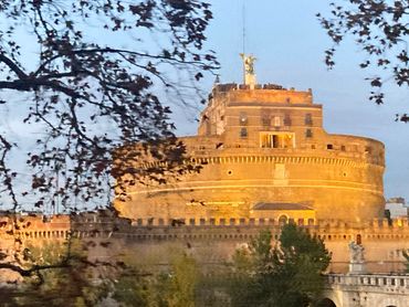 Castle Sant'Angelo illuminated at dusk with tree branches in foreground.