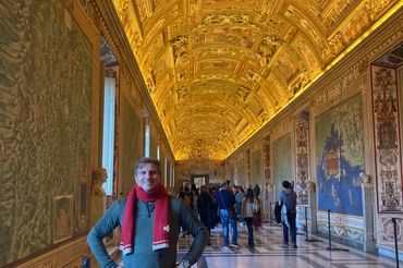 Man posing in an ornately decorated museum hallway with a golden ceiling.