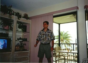 Man smiling indoors near sliding glass door with tropical view outside.