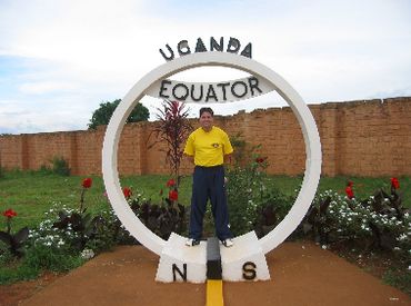 Man standing at Uganda's equator marker with north and south directions.