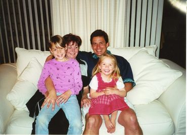 A happy family of four sitting closely on a white couch.