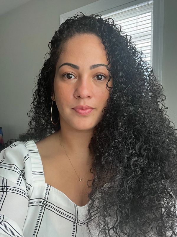 Woman with curly hair wearing a white checkered top and gold hoop earrings.