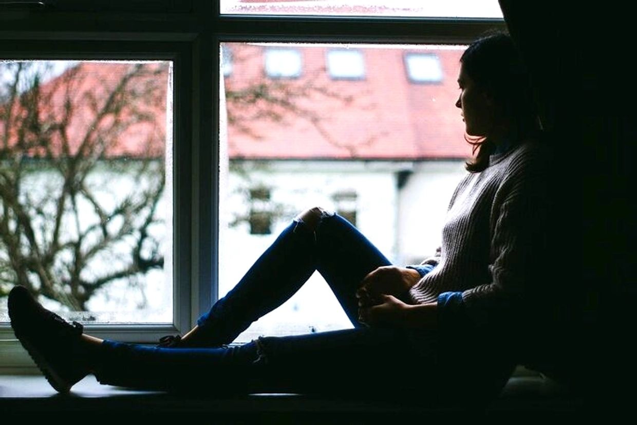 Silhouette of a woman sitting by a window looking outside.