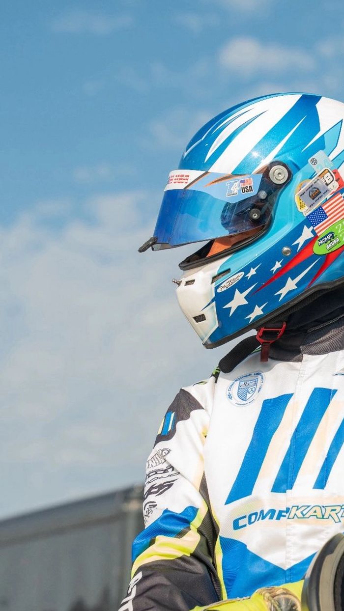Kart racer in a blue and white helmet with yellow gloves prepares for a race.