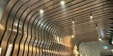 Curved wooden slats form a wavy ceiling design with recessed lights.