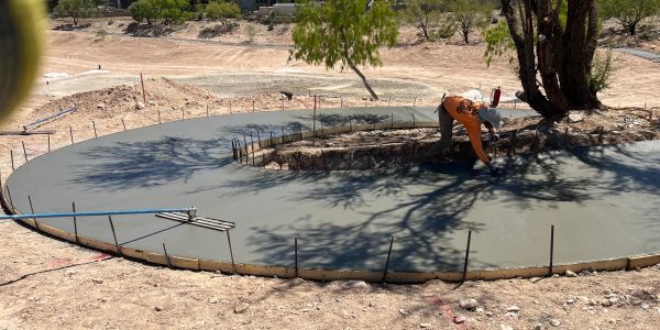 Worker smoothing fresh concrete around a tree.
