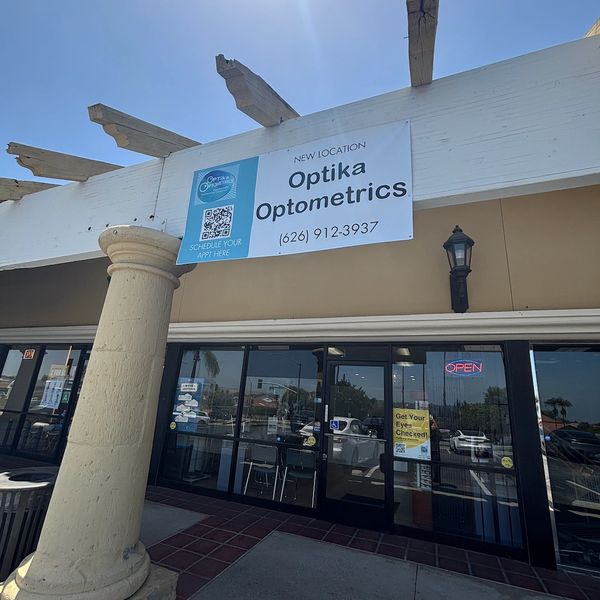 Optika Optometrics storefront with new location sign and open neon light.