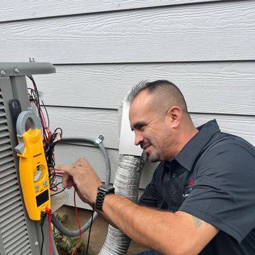 Technician testing an HVAC unit with a multimeter outdoors.