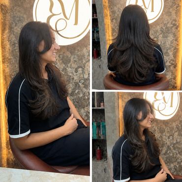 Woman showcasing long, layered haircut with soft curls at a salon.