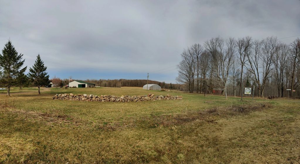 Rural landscape with a stone wall, open field, and bare trees under a cloudy sky.