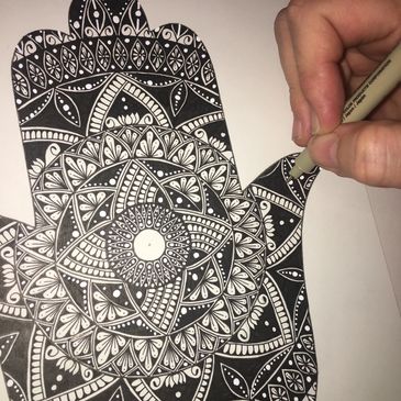 The artists hand is shown drawing a black and white Hansa mandala