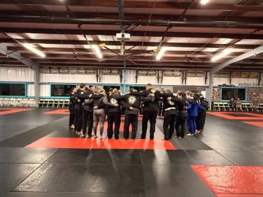 A martial arts group huddles in a circle on a mat, showing team unity.