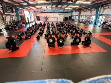 Martial arts class with students seated in rows facing instructors in a gym.