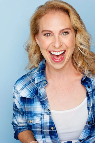 Joyful woman with blonde hair wearing a blue plaid shirt laughing heartily.
