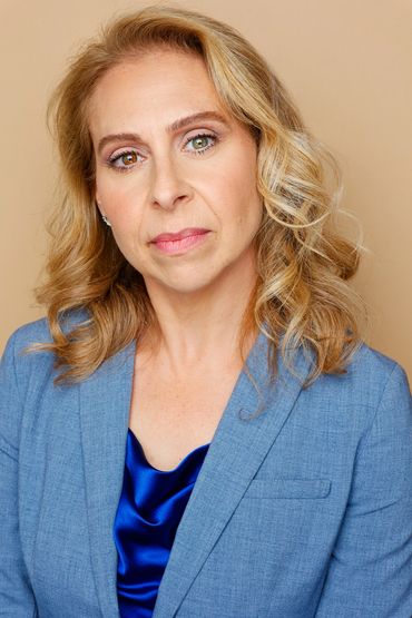 Portrait of a serious woman in a blue blazer and satin blouse.