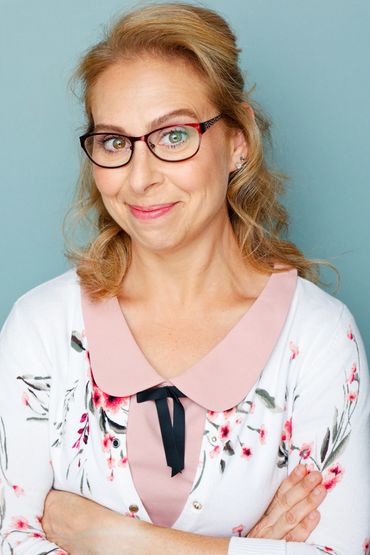 Smiling woman with glasses wearing a floral cardigan and pink blouse.