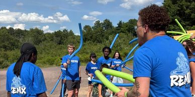 Group activity with people holding pool noodles outdoors.
