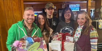 Group of five smiling people holding gift packages indoors.