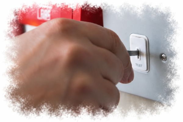 Hand pressing a test switch on a fire alarm panel.