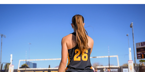 Female volleyball player wearing jersey number 26 stands on the court with a clear blue sky.