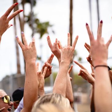 Hands raised in the air showing peace and victory signs at an outdoor event.