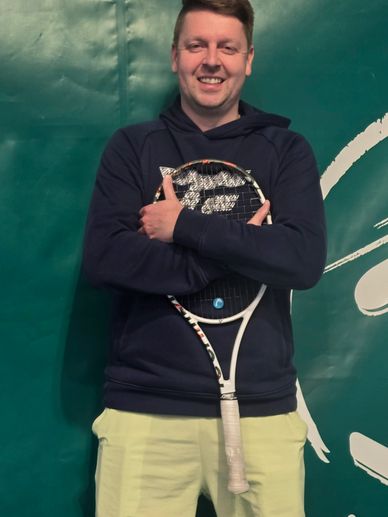 Smiling man holding a tennis racket against a green background.