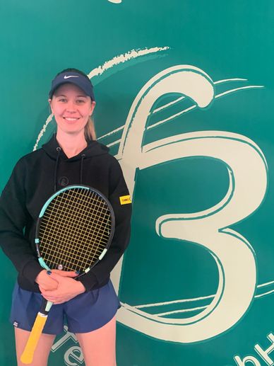 Young woman in tennis attire holding a racket, smiling.