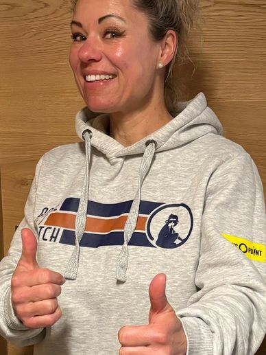 Smiling woman giving two thumbs up wearing a light grey hoodie.