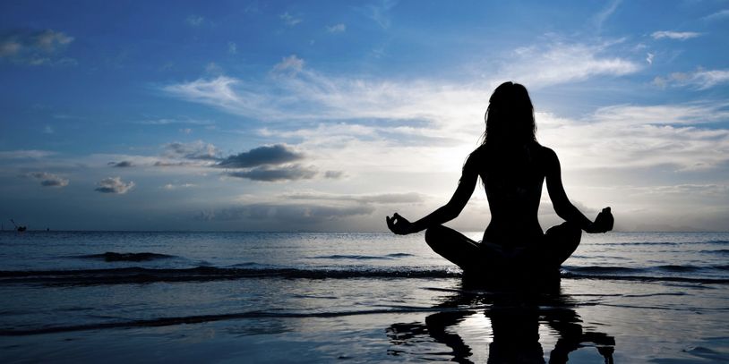 A person meditating on the shore of the ocean.