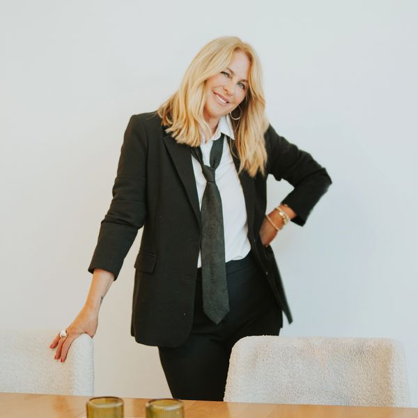 Femme blonde souriante en costume noir décontracté.