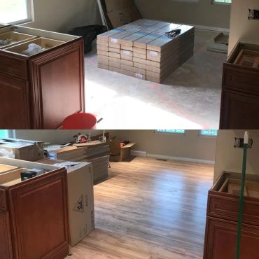 Room under renovation with new laminate flooring and kitchen cabinets.