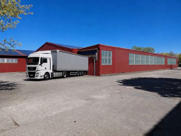 Weißer LKW vor rotem Lagergebäude.