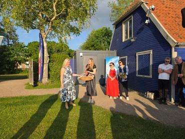 People gathered outdoors near a blue house on a sunny day.